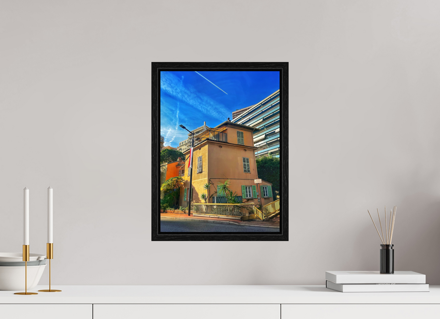 Framed street scene photo print in black floater frame, featuring a yellow building corner and sky.