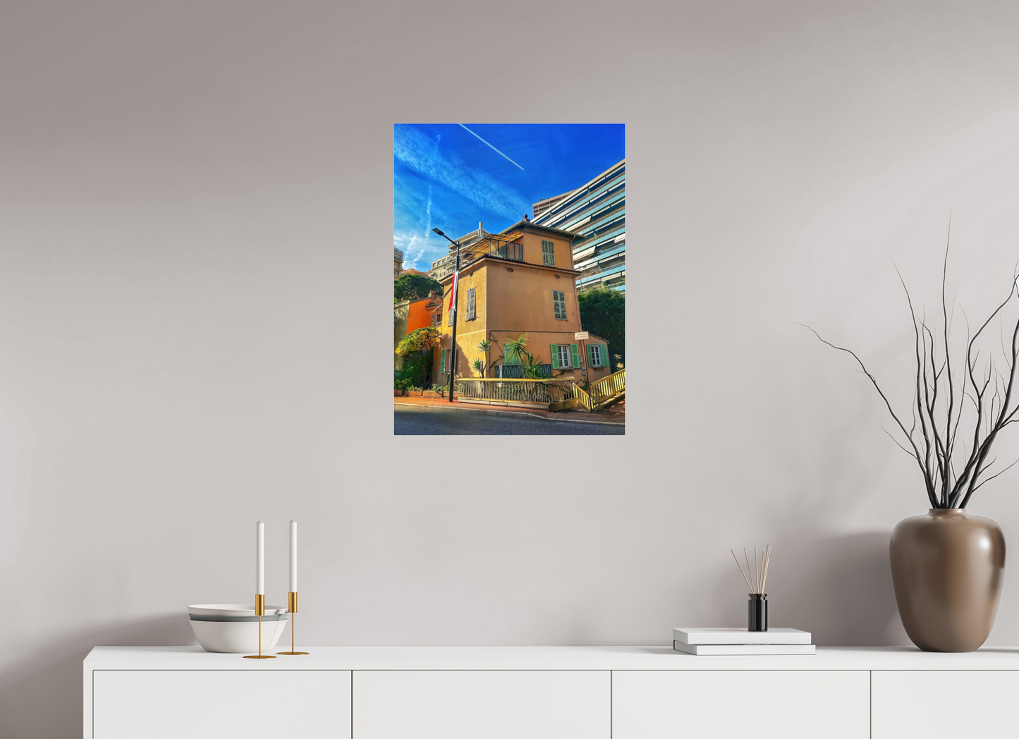 Square framed photo print under acrylic glass showing a yellow house with windows, balcony, and blue sky.