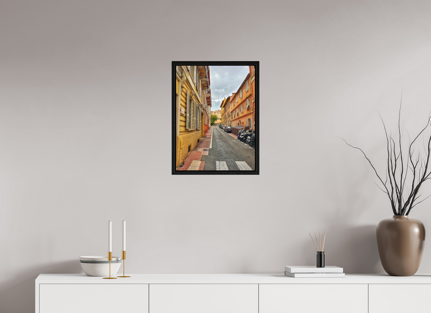 Square framed photo print with a black frame, depicting a narrow street with bright building walls