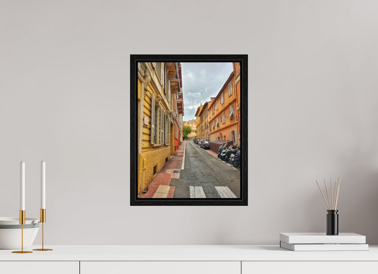 Square framed photo print of a sidewalk alley between colorful buildings under a cloudy sky