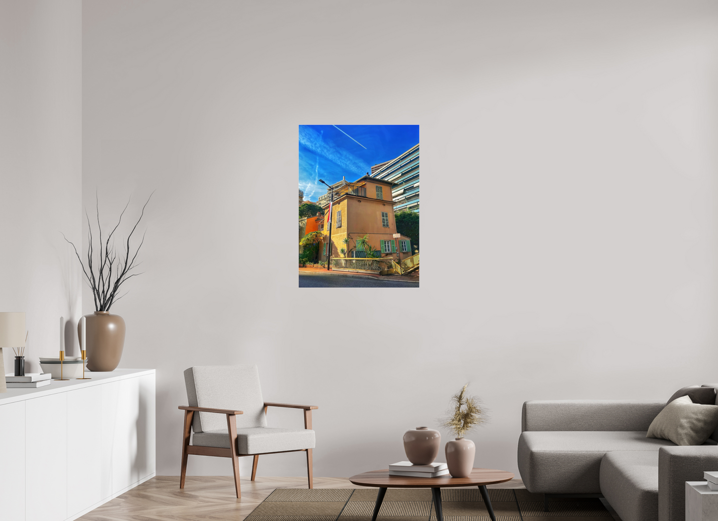 Square framed photo print under acrylic glass showing a yellow house, greenery, and vivid blue sky.