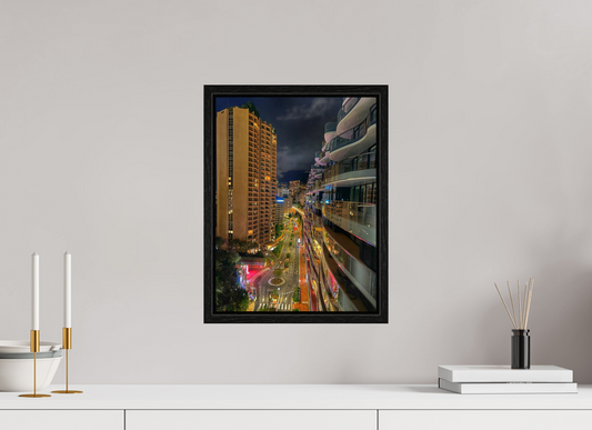 Square black-framed photo print of a nighttime city street with tall buildings and colorful lights