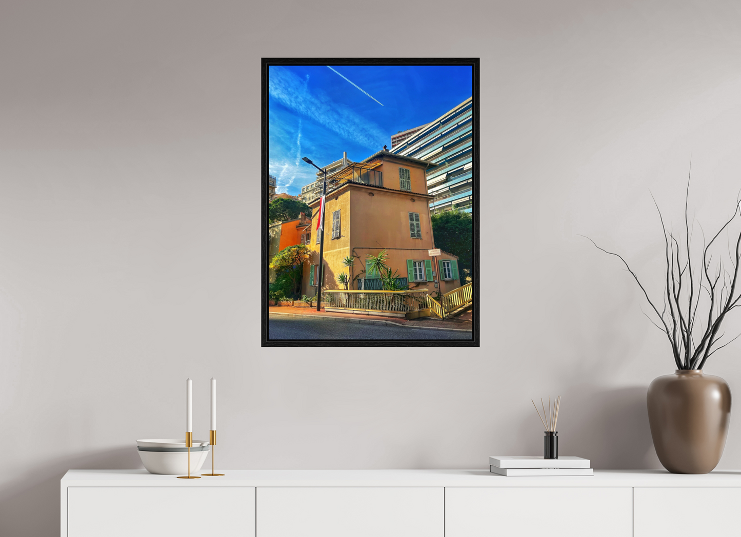 Framed street scene photo print in black floater frame, showing a yellow building under blue sky.